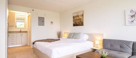 A bedroom with a bed, bedside table, lamp, and a grey sofa.