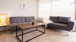 A modern living room with a grey sofa, a wooden coffee table, and a large window providing natural light. - Stylish 1BR Escape in Kissimmee, minutes to Disney (Kissimmee)