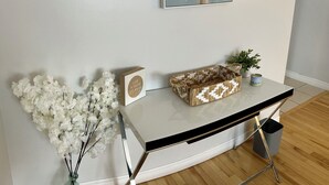 Una habitación moderna con una consola de mármol blanco, una cesta decorativa, una pequeña planta en maceta y un cuadro en la pared.