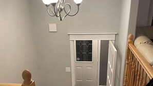 Una escalera con barandillas de madera, un candelabro y una puerta con un diseño geométrico de vidrio.