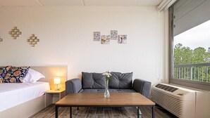 Ein Hotelzimmer mit einem Bett, einer Couch, einem Tisch mit einer Vase, einem Nachttisch, Wandbildern und einem Fenster mit Aussicht.
