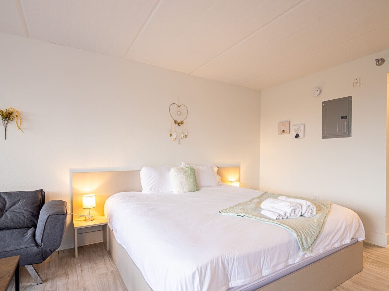 Een hotelkamer met een groot bed, een nachtkastje met een lamp, een stoel en een hartdecoratie aan de muur.