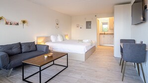A modern, well-lit room with a sofa, a bed, a coffee table, and a TV mounted on the wall. - Kissimmee 1BR Cottage W/Lake view & Next to Disney (Kissimmee)