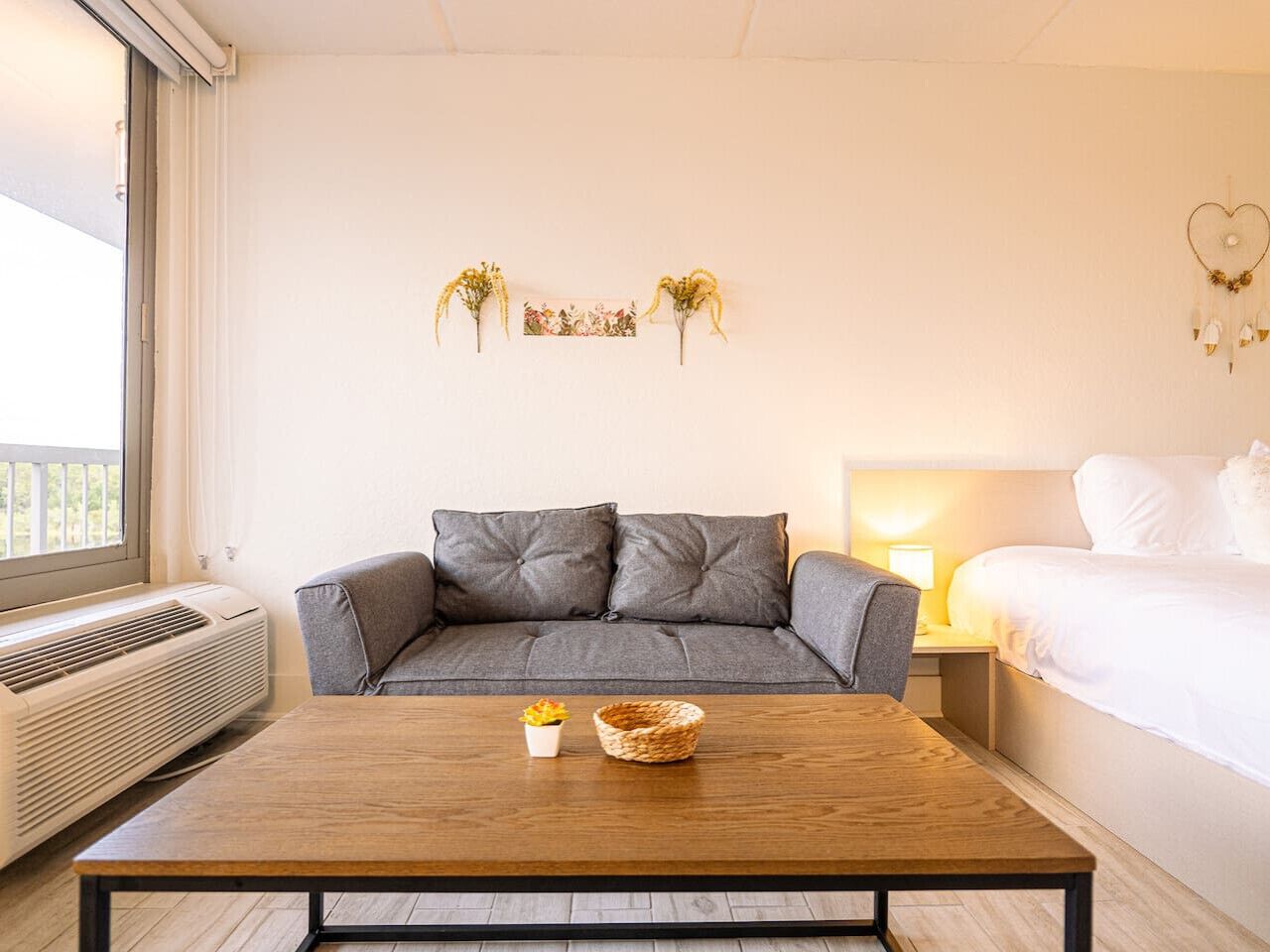 Een moderne slaapkamer met een grijze bank, een houten salontafel, een nachtkastje met een lamp en een bed met witte lakens.