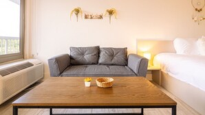 A modern bedroom with a grey sofa, a wooden coffee table, a bedside table with a lamp, and a bed with white linens. - Kissimmee 1BR Cottage W/Lake view & Next to Disney (Kissimmee)
