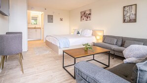 A modern, well-lit living room with a bed, a sofa, a coffee table, and a dining area.