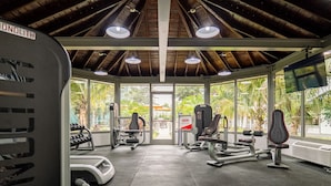 A gym with various exercise equipment, large windows, and a view of greenery outside.