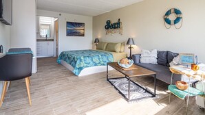 Ett kompakt bostadsutrymme med en säng, en soffa och en liten matplats. Ett kök syns i bakgrunden.