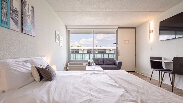 Habitación de hotel con una cama grande, un escritorio y un balcón con vistas a la ciudad.