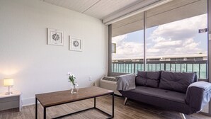 A modern living room with a wooden coffee table, a gray sofa, and a large window offering a view of a bridge.