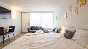 Een moderne hotelkamer met een groot bed, een bureau en een slaapbank. Een raam zorgt voor natuurlijk licht.
