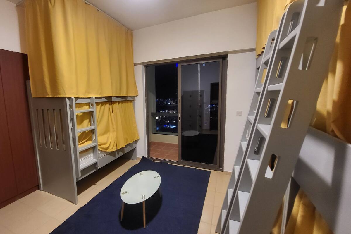 Quarto com beliche, uma mesinha, guarda-roupa e porta de vidro deslizante para uma varanda com vista para a cidade.