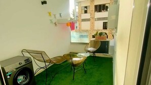Un ambiente compatto con lavatrice, due sedie, un tavolino e vista su un edificio con facciata in mattoni.