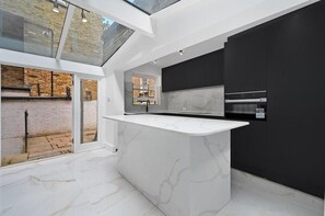 Una cocina moderna con una isla de mármol, armarios negros y un tragaluz.
