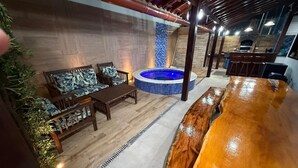 A cozy indoor seating area with a wooden table and chairs, a hot tub, and a tiled wall. - Casa Carneiros 4QTS-JacuzziEChurrasq 039 (Tamandaré)