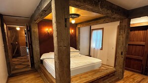 Un dormitorio rústico con vigas de madera a la vista, suelo de madera, una cama y una araña.