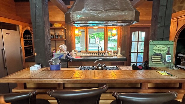 Una cocina rústica con una isla grande, taburetes de bar y vistas a través de las ventanas.