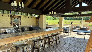 Zona de bar al aire libre con mostrador de piedra, taburetes de madera y vista a un paisaje verde.