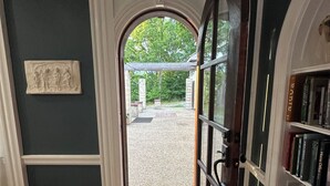 Una habitación con piso de madera, una estantería, una puerta que da a un área exterior con pérgola y una escultura en la pared.