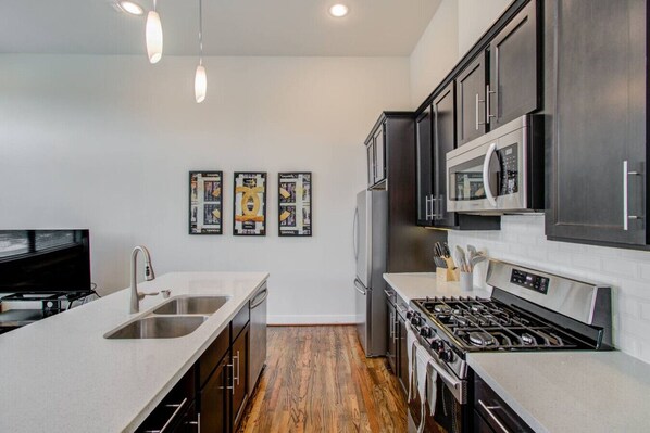 A modern kitchen with a central island, stainless steel appliances, and a wooden floor.