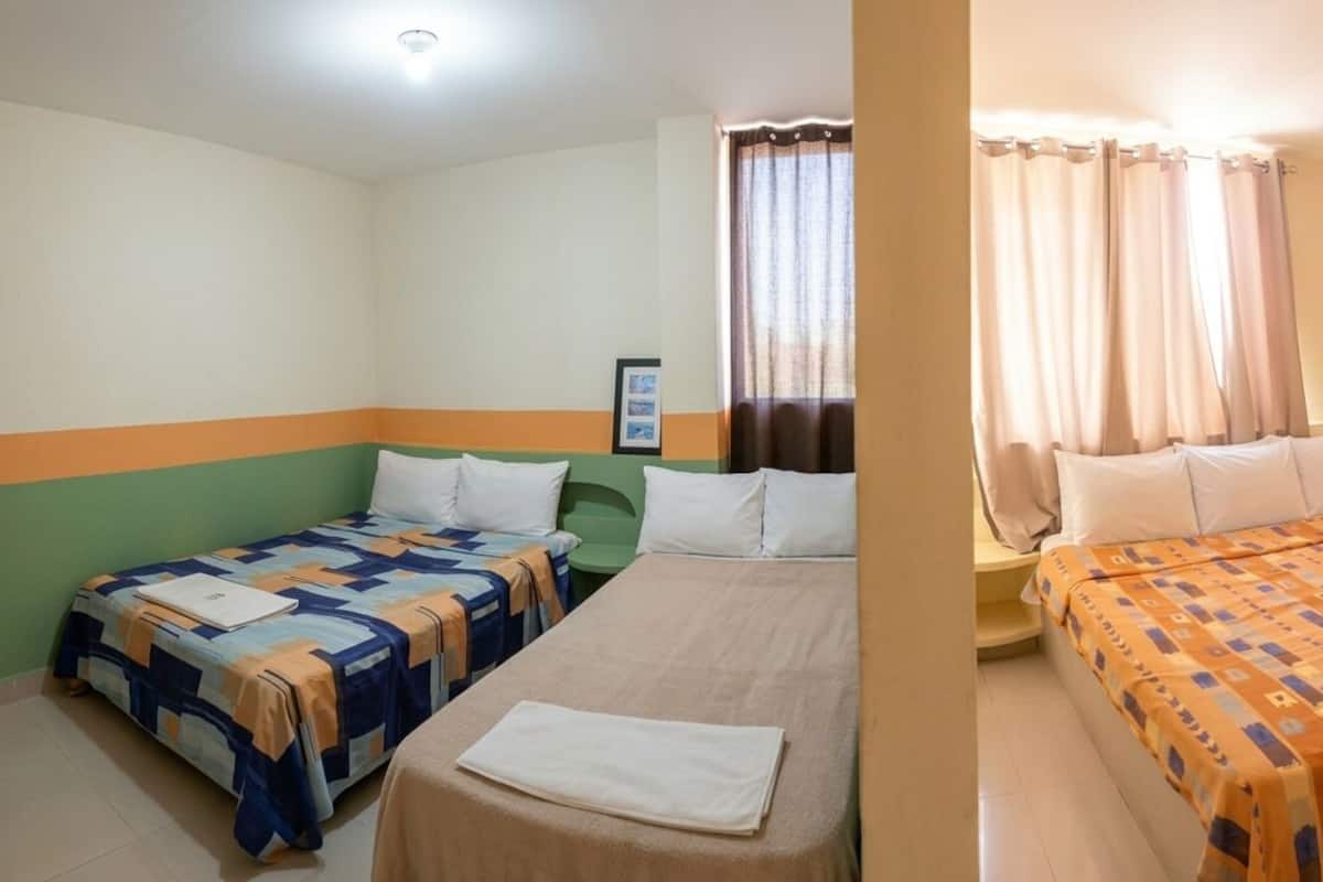Une chambre avec deux lits, un mur vert et orange, une fenêtre avec des rideaux et un appareil de climatisation.