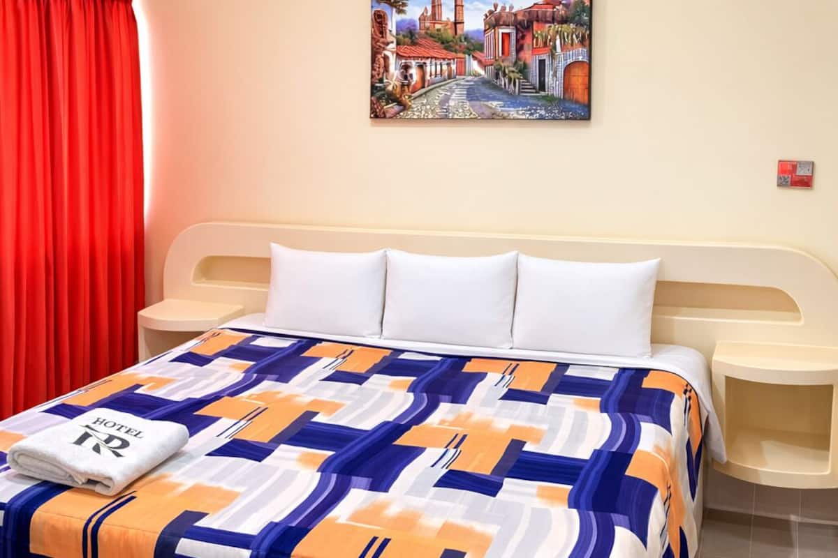 Une chambre d’hôtel avec un lit, un tableau au mur et un rideau rouge.