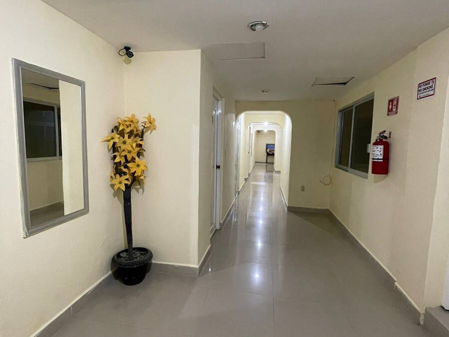 Un pasillo largo y bien iluminado con un extintor y un cartel de 'No Fumar' en la pared.