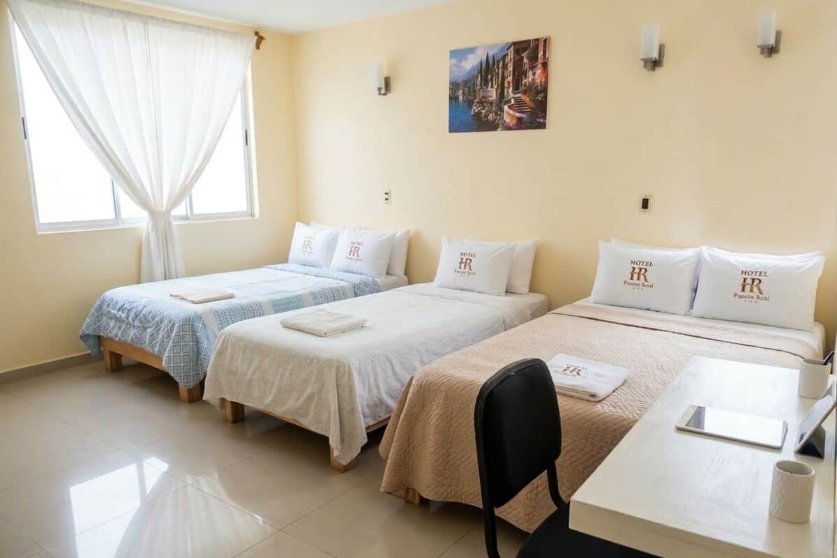 Une chambre d’hôtel avec trois lits, un bureau et une chaise.