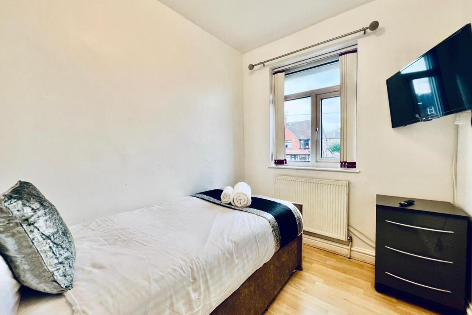 A bedroom with a bed, a dresser, a window, and a TV.