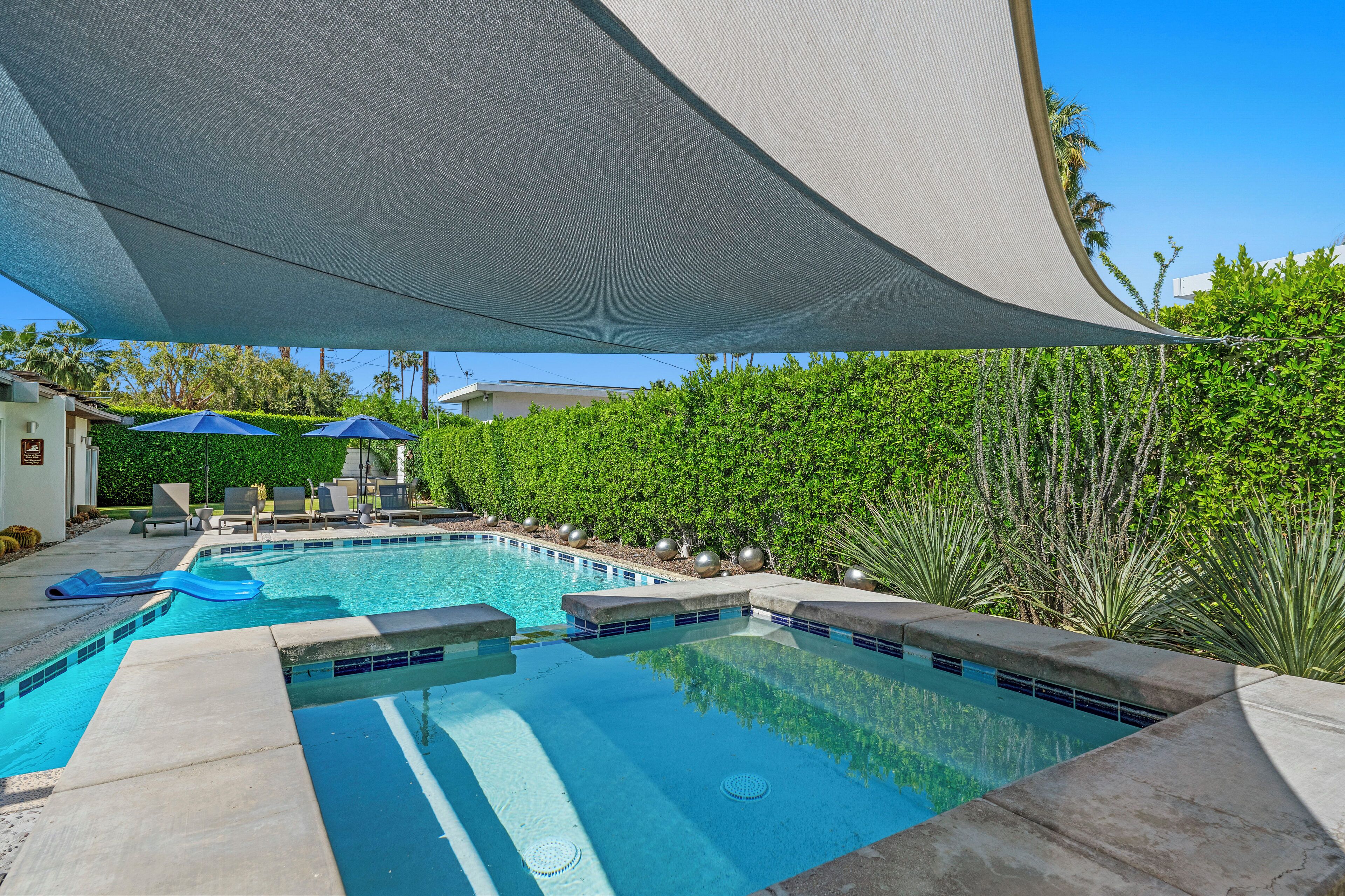 Una piscina con zona sombreada, sillas de descanso y un cielo azul despejado.