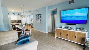 Una sala de estar con televisor, sofá, reposapiés y un comedor con sillas y una mesa.