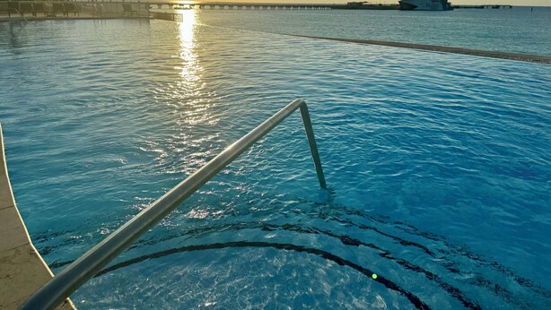 Una piscina con el sol reflejado en el agua, un muelle al fondo y un barco amarrado en el muelle.