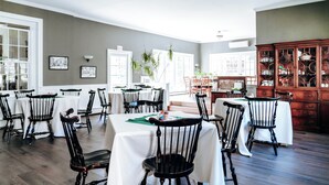 Un espace repas comprenant plusieurs tables et chaises, un buffet en bois doté de portes en verre, et des tableaux encadrés accrochés aux murs.