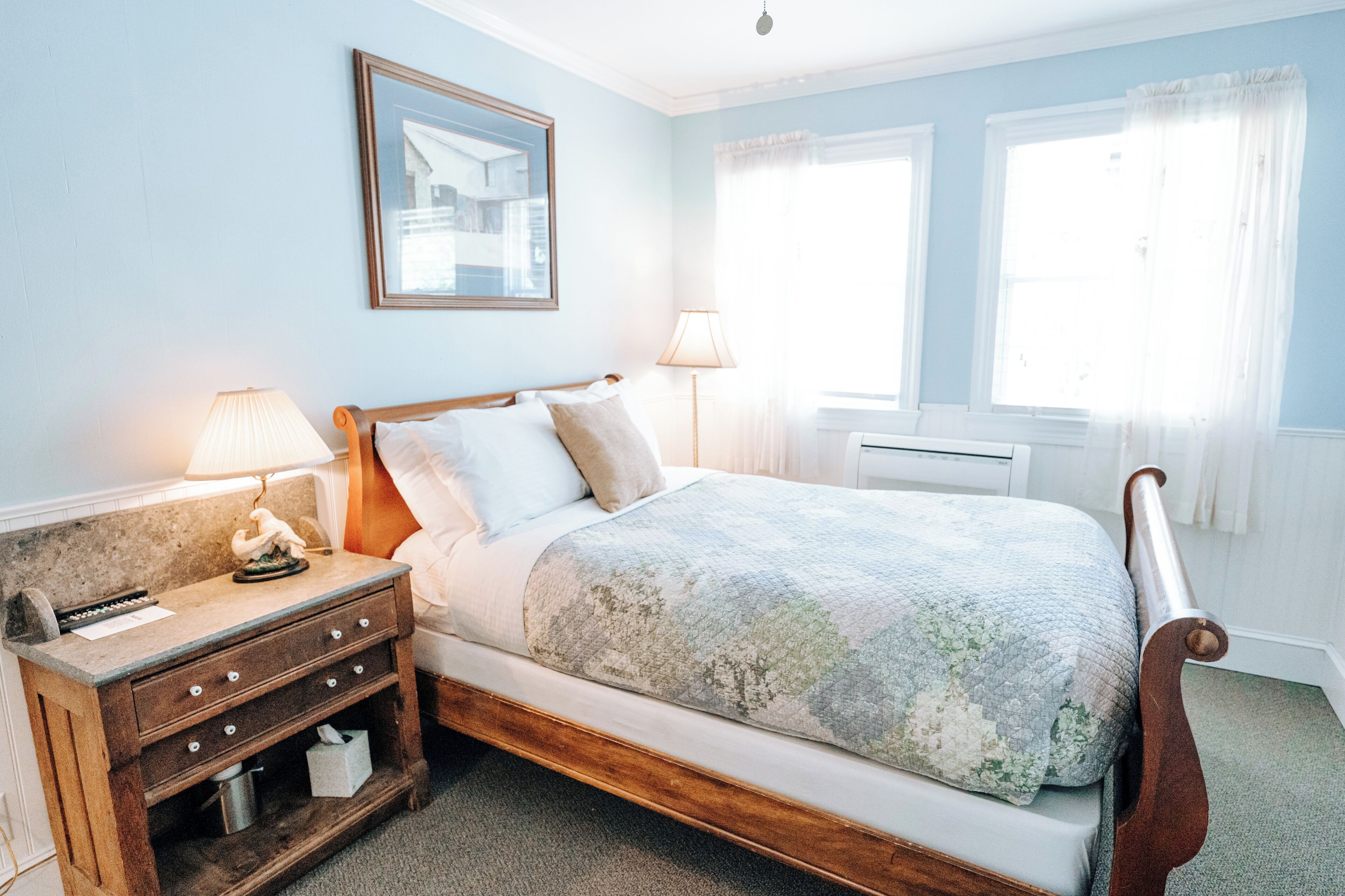 A bedroom with a bed, nightstand, lamp, and a framed picture on the wall.