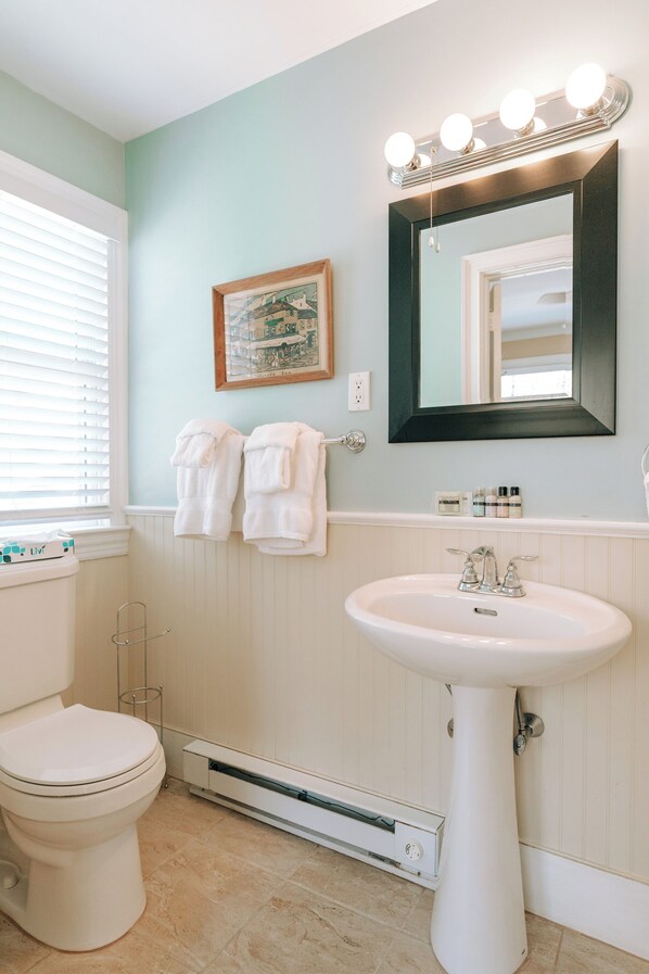 Un baño con inodoro blanco, lavamanos pedestal y espejo con luces.