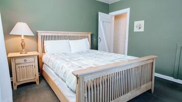 A bedroom with a wooden bed, a nightstand with a lamp, and a door leading to a bathroom.