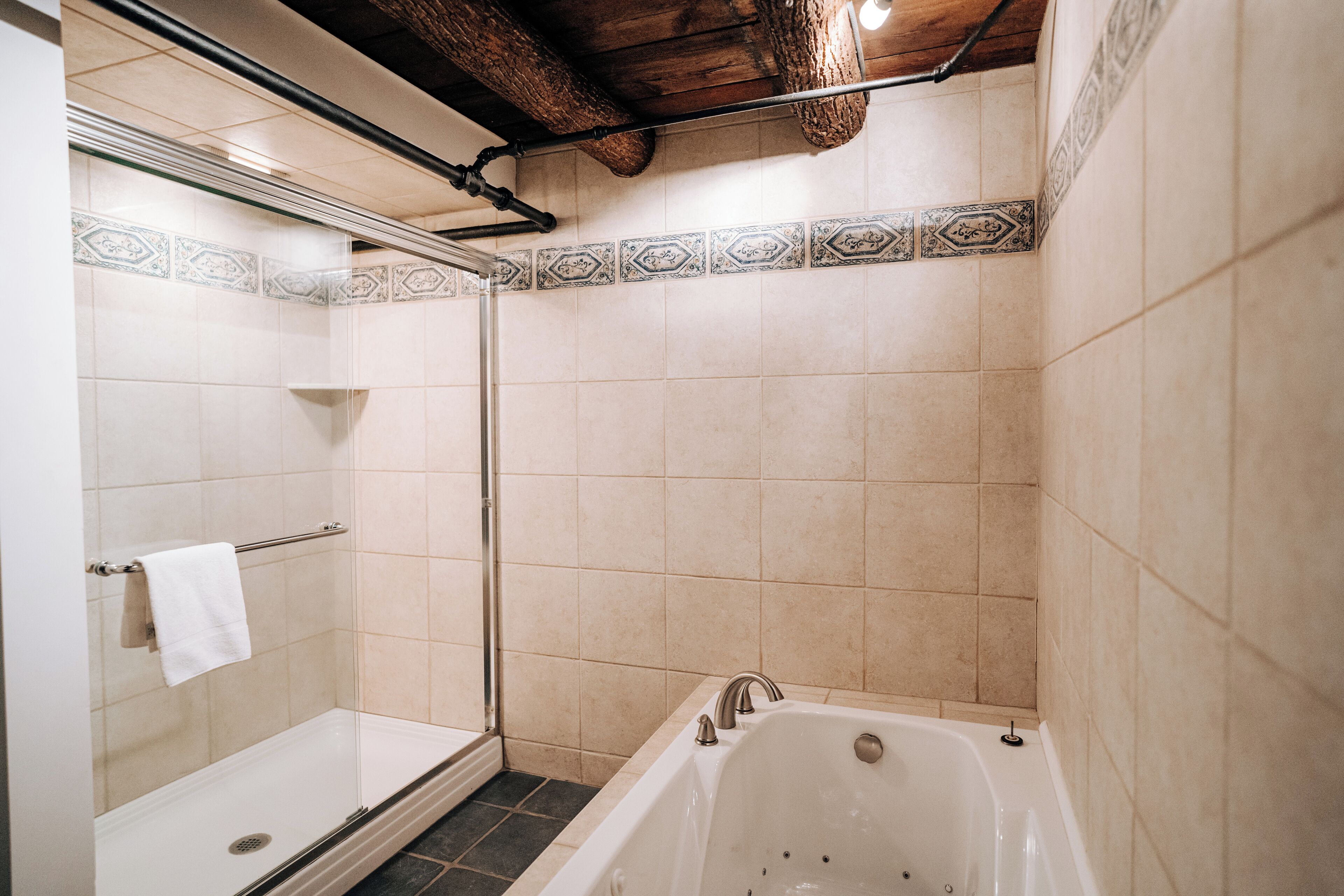 A bathroom with a glass-enclosed shower, a white bathtub, and patterned tiles.