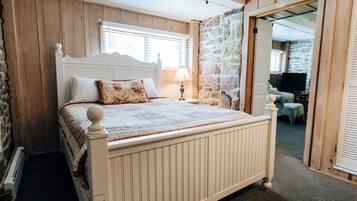 A bedroom with a wooden bed, a stone wall, and a television in the corner.