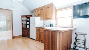 Une cuisine avec des meubles de rangement en bois, un réfrigérateur blanc, un îlot central en bois et un tabouret de bar.