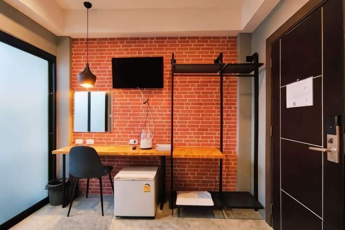 Ein Zimmer mit Backsteinwand, Schreibtisch mit Stuhl, Fernseher über dem Schreibtisch montiert und eine Tür mit Schloss.