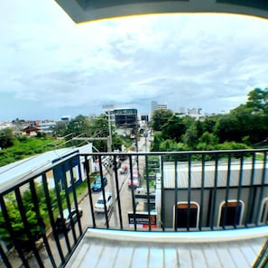 A view from a balcony overlooking a street with buildings, cars, and greenery.