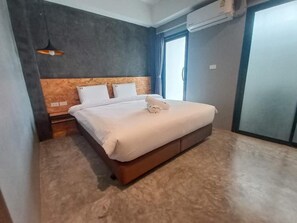 A hotel room with a bed, a nightstand, a wall-mounted air conditioner, and a window with curtains. - Modern Budget Hotel Hatyai Thailand (Hat Yai)