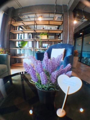Un intérieur moderne avec une bibliothèque aux étagères incurvées, un fauteuil bleu et un plant de lavande en pot posé sur une table en verre.
