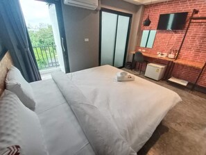 Et hotelværelse med seng, skrivebord, fjernsyn og en balkon.