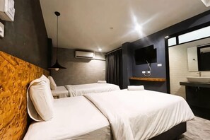 Une chambre d’hôtel avec deux lits, une tête de lit en bois, un téléviseur fixé au mur, un climatiseur mural et une salle de bain avec un lavabo et un miroir.