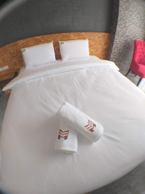 A bed with white linens and two pillows, a wooden headboard, and a red chair in the background.