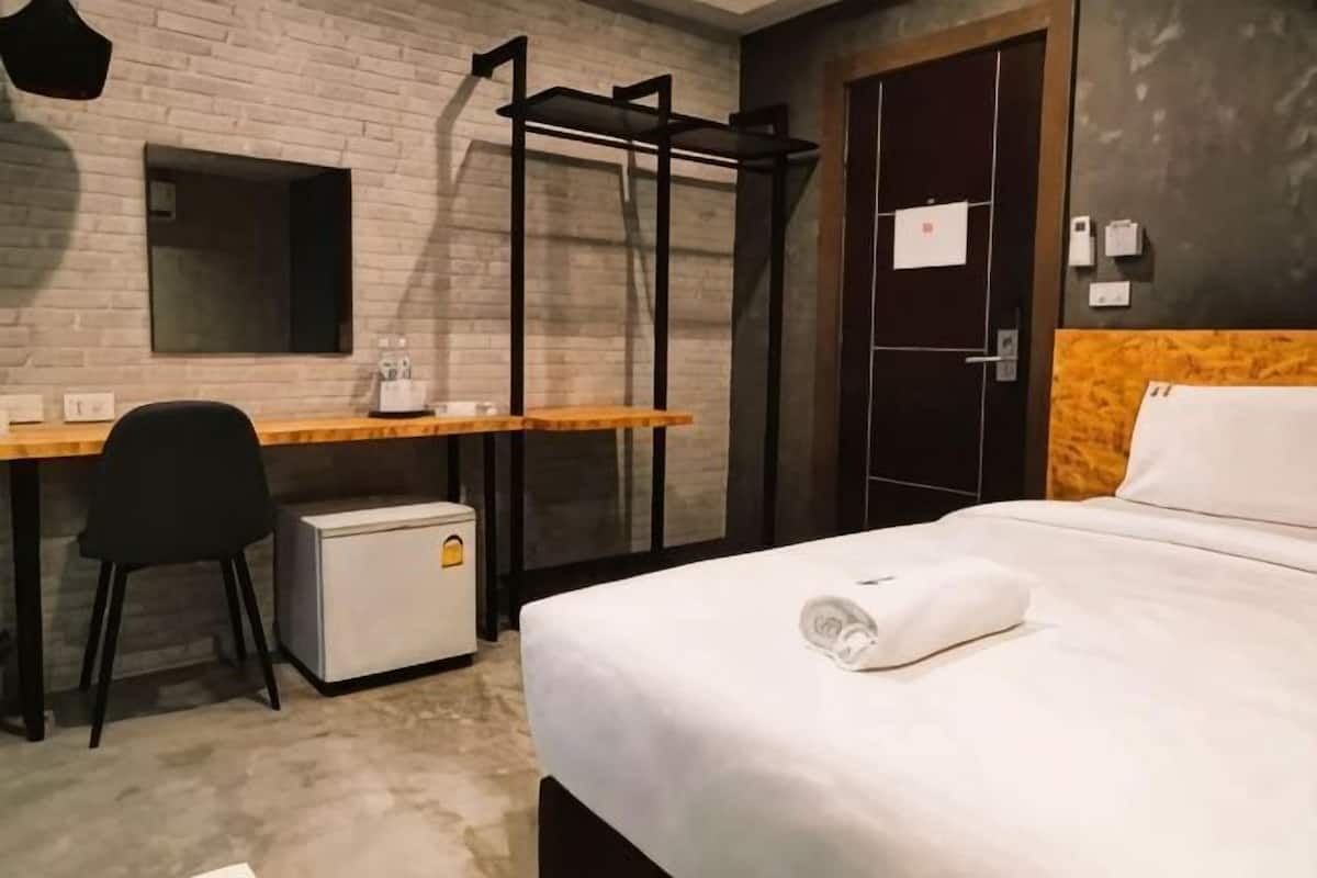 Ein Hotelzimmer mit Bett, Schreibtisch, Stuhl, kleinem Kühlschrank und Spiegel.