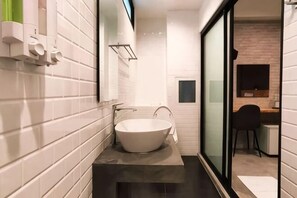 Un baño moderno con azulejos blancos, un lavamanos grande y un mamparo de vidrio.
