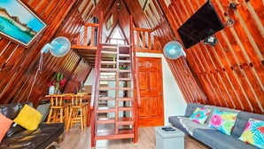 Een gezellige zolderkamer met een houten trap, een bank, een eettafel en twee ventilatoren.