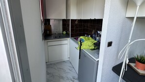 Une cuisine compacte avec des meubles blancs, un petit plan de travail et un four à micro-ondes. On y trouve un évier avec un robinet, un petit réfrigérateur et une plante en pot sur le plan de travail.